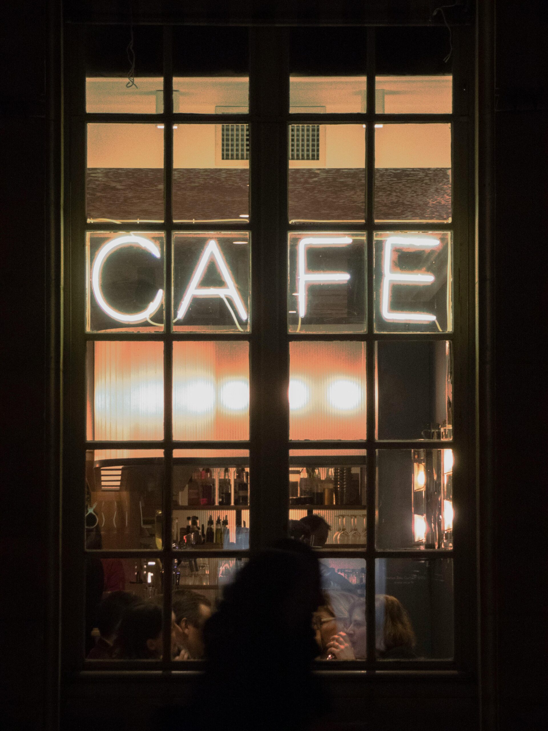 Night view of a bustling Paris café through a window with a bright neon sign.